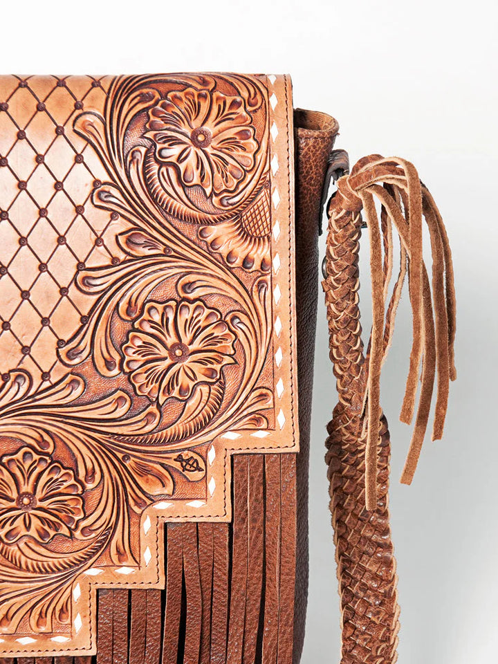 Close-up of a leather bag with intricate tooled design and braided handle on a white background