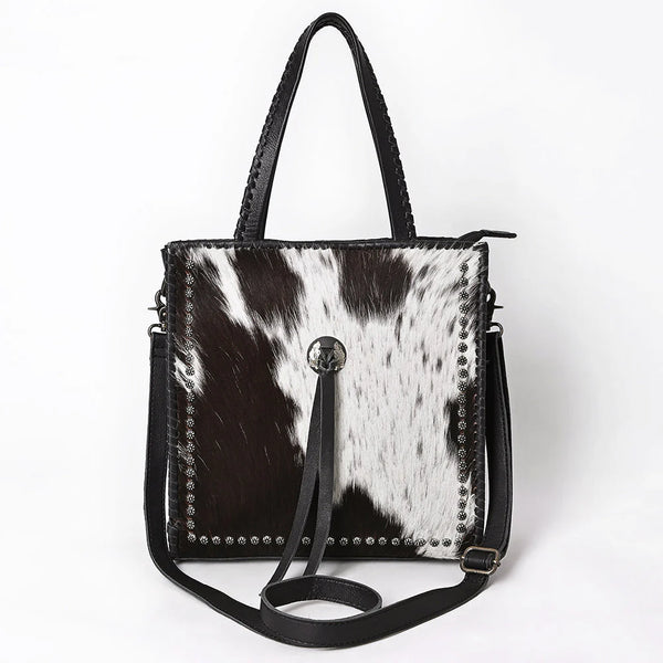 Front view of ADBG1751 black and white cowhide leather tote bag with silver studs and Western concho tassel.