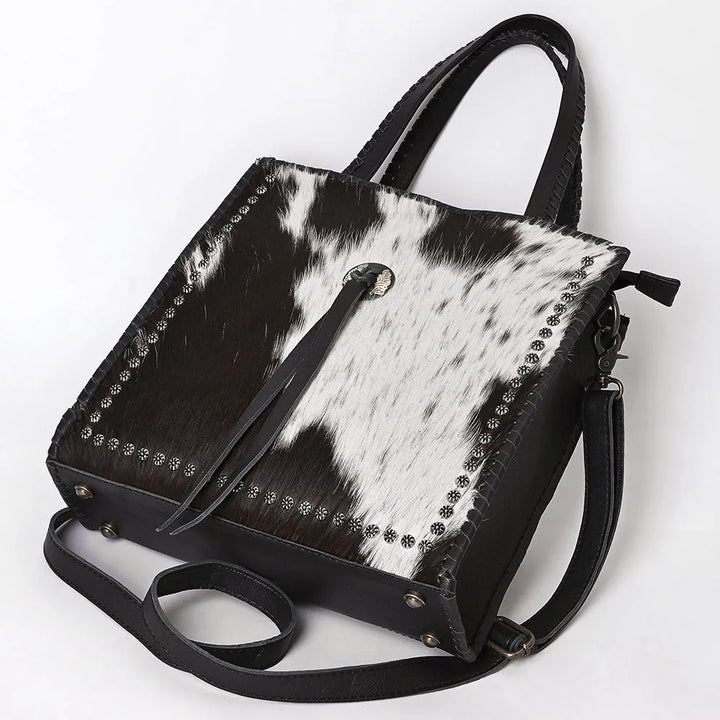 Front of black and white cowhide tote bag showing full-grain leather back panel and Western craftsmanship.  
